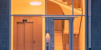 Modern building entrance with illuminated staircase and elevator inside.