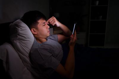 Young man using smartphone in bed at night.
