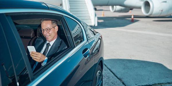 Businessman in a car at the airport looking at his phone.