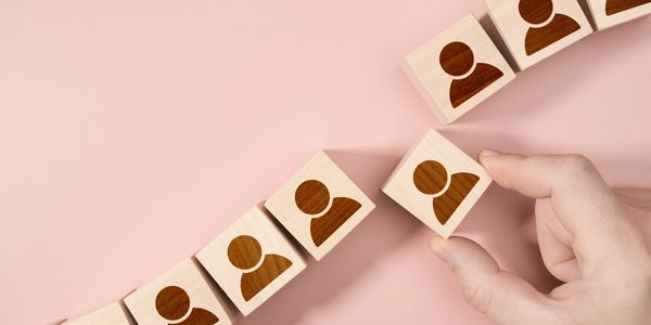 Hand placing a wooden block with a person icon among others in a rising pattern.