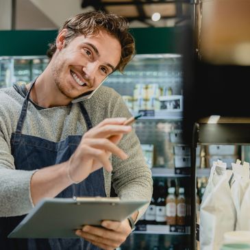 Smiling store employee multitasking with phone and clipboard in a grocery store.