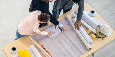 Three professionals reviewing architectural plans on a table with safety helmets and coffee cups.