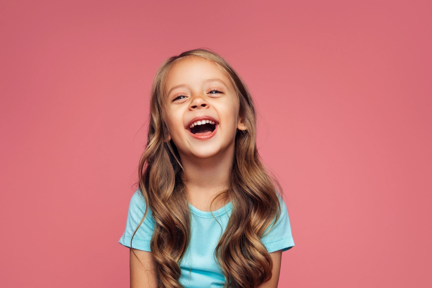 Happy young girl laughing against a pink background.