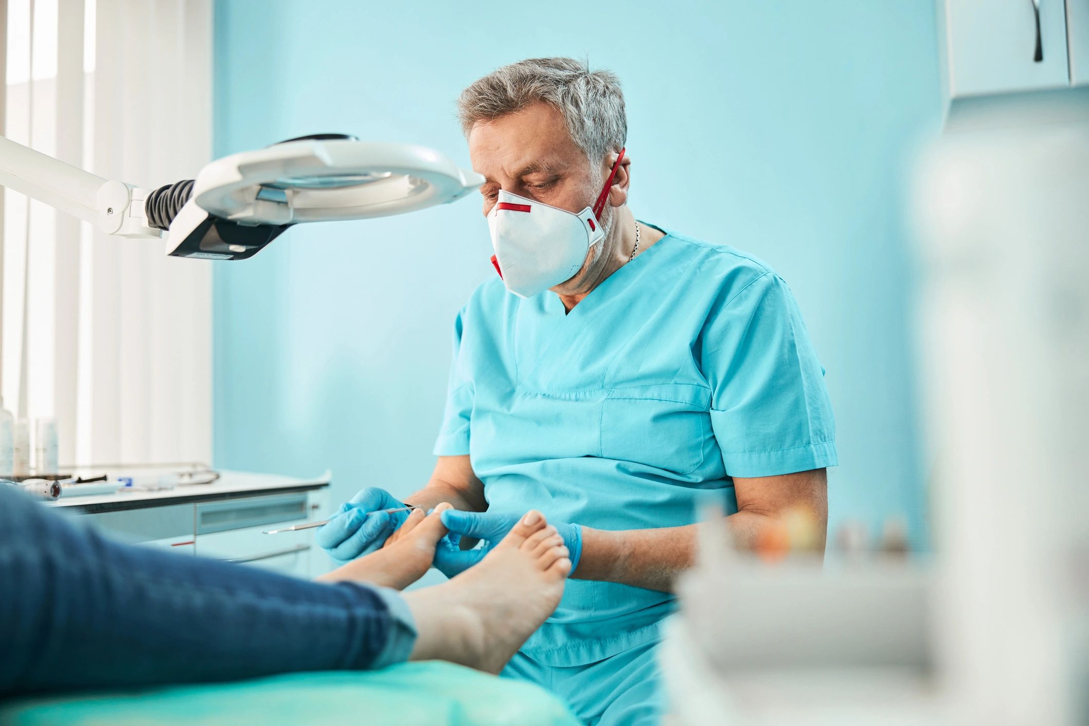 Podiatry professional wearing a mask and gloves while examining a patient’s feet.