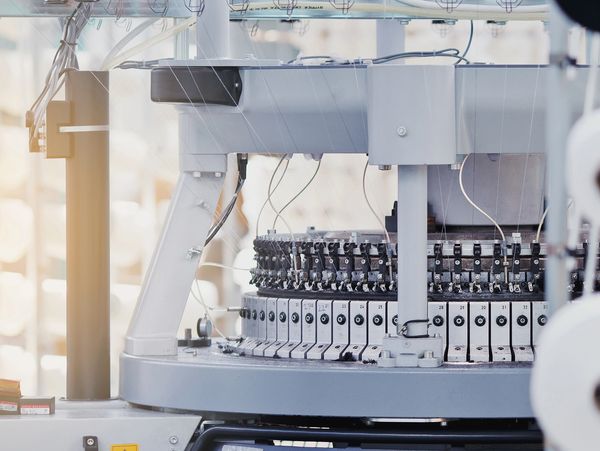 Close-up of textile machinery with spools and threads in a factory.
