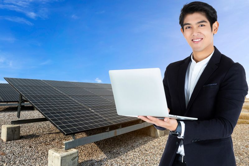 Businessman or engineer working with laptop computer with power solar panel on blue sky background,alternative clean green energy concept