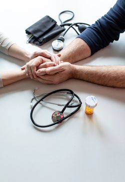 Patient and doctor holding hands during consultation with medical tools on table.