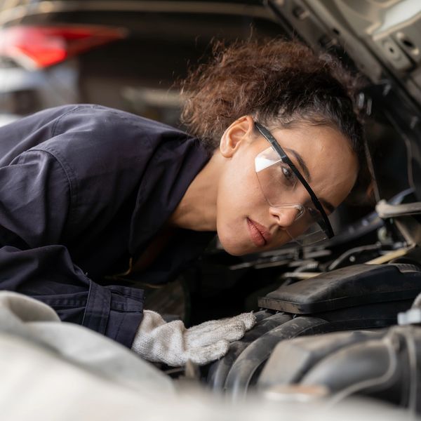 Woman mechanic inspecting a car engine with safety glasses and gloves.