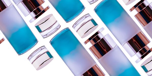 Assorted frosted blue and clear cosmetic bottles with silver caps on a white background.