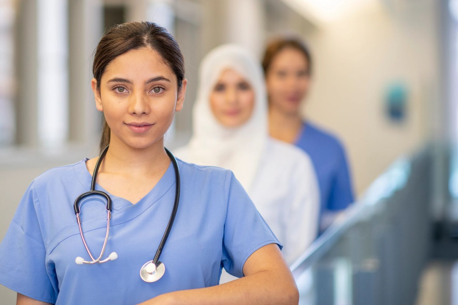 Confident female healthcare professional with colleagues in hospital corridor.