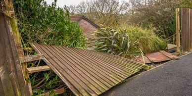 Broken wooden fence panels lying on the ground beside a road.