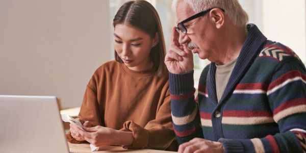 Young woman helping an elderly man with finances using laptop.