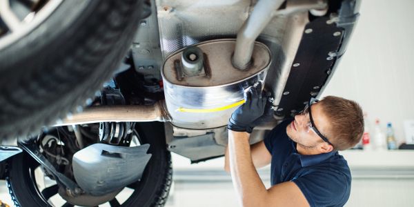Mechanic inspecting a car's exhaust system underneath the vehicle.