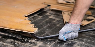Hand removing wooden flooring with crowbar.