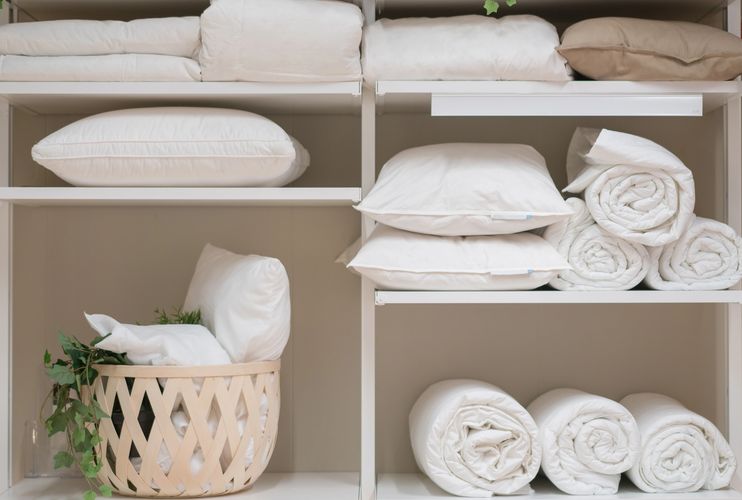 Neatly organized white pillows and rolled blankets on shelves with a basket.
