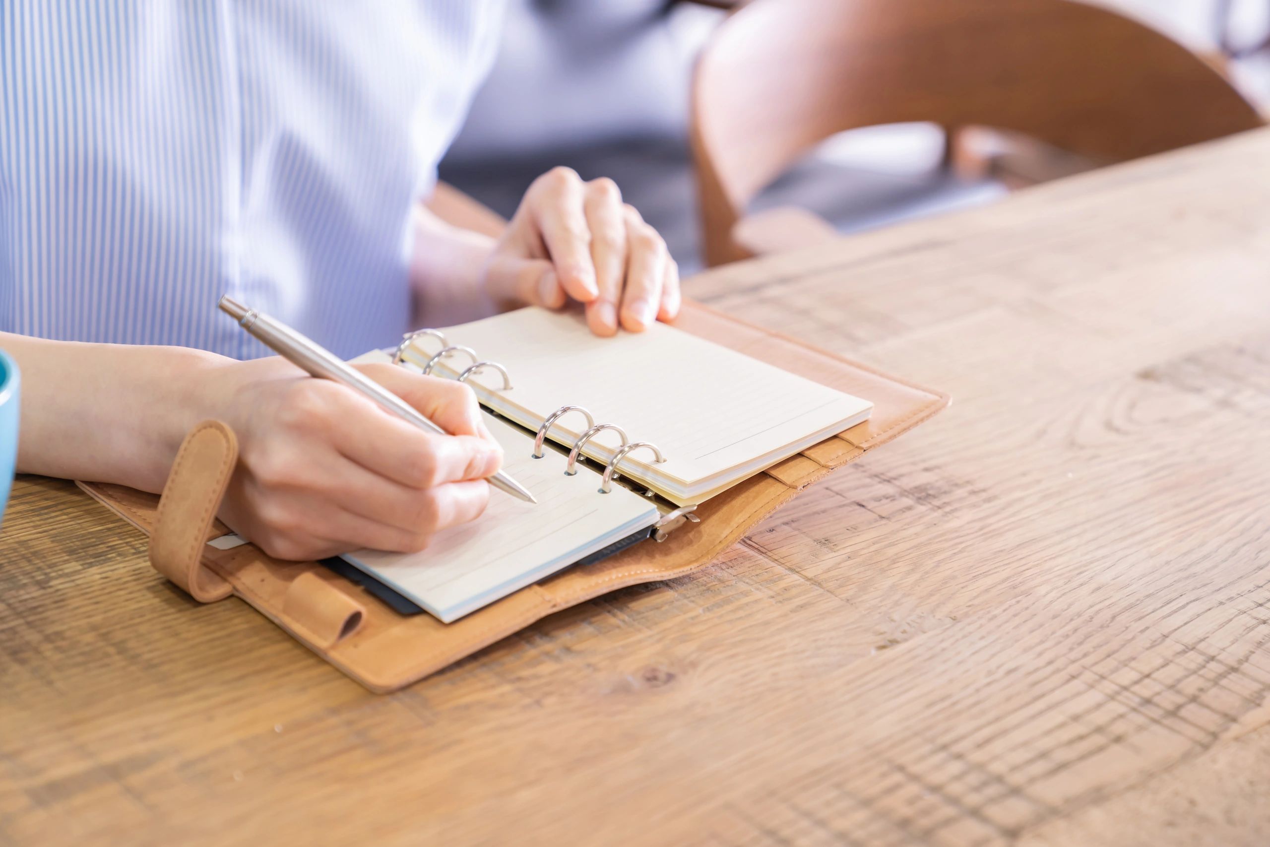 Person writing in an open leather-bound planner with a pen.