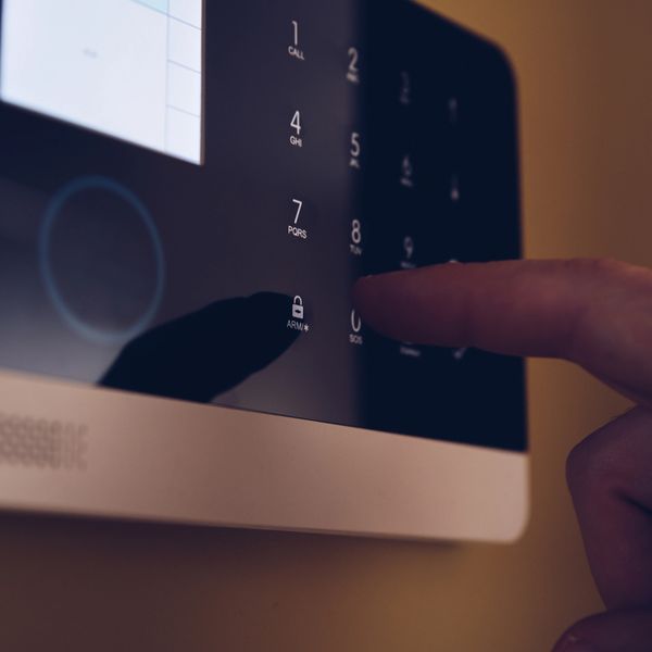 Finger pressing a button on a security alarm keypad.