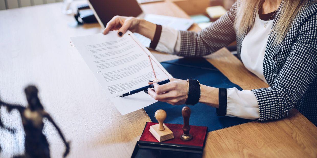A woman reviews and points at a legal document with a pen in an office setting.