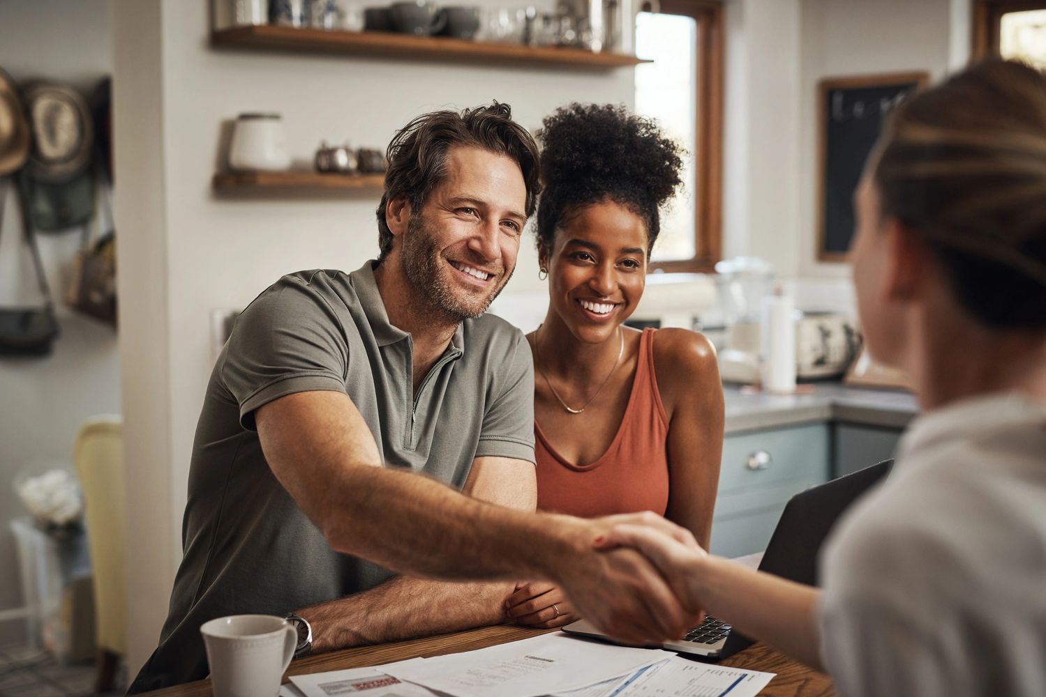 Happy couple shaking hands with a professional in a cozy kitchen setting.