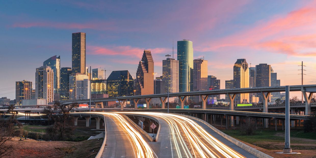 City skyline with light trails on highways at sunset.