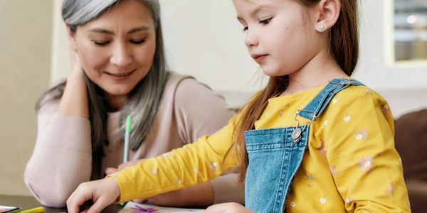 Young girl painting while an older woman watches with a smile.