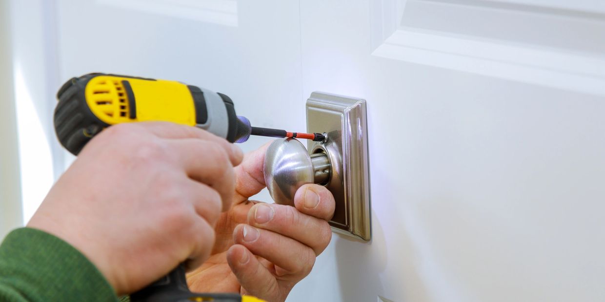 Person using a drill to install a door knob on a white door.
