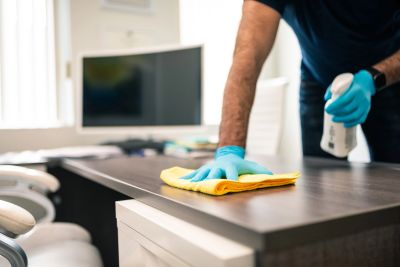 Person cleaning desk with spray and cloth.