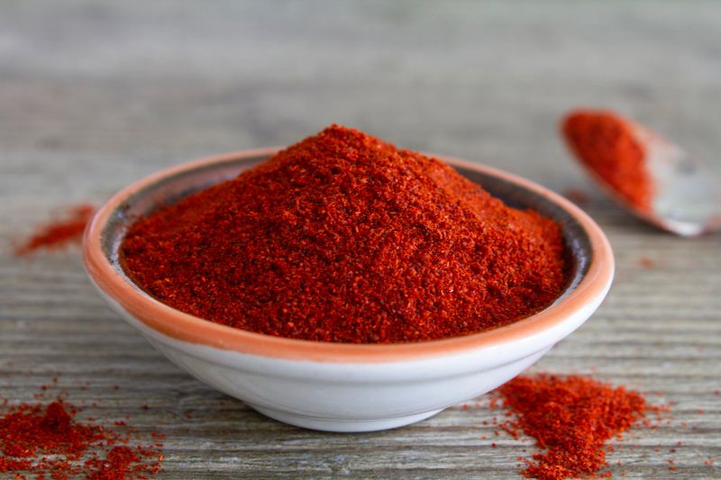 Paprika spice in a small dish on a rustic wooden grey table. Close up view with copy space. Stock photo.