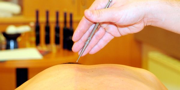 Hand holding a massage tool above a person's back in a spa setting.