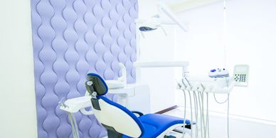 Modern dental clinic room with blue and white dental chair and equipment.