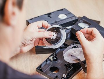Person repairing a VHS tape by handling the tape reels carefully.