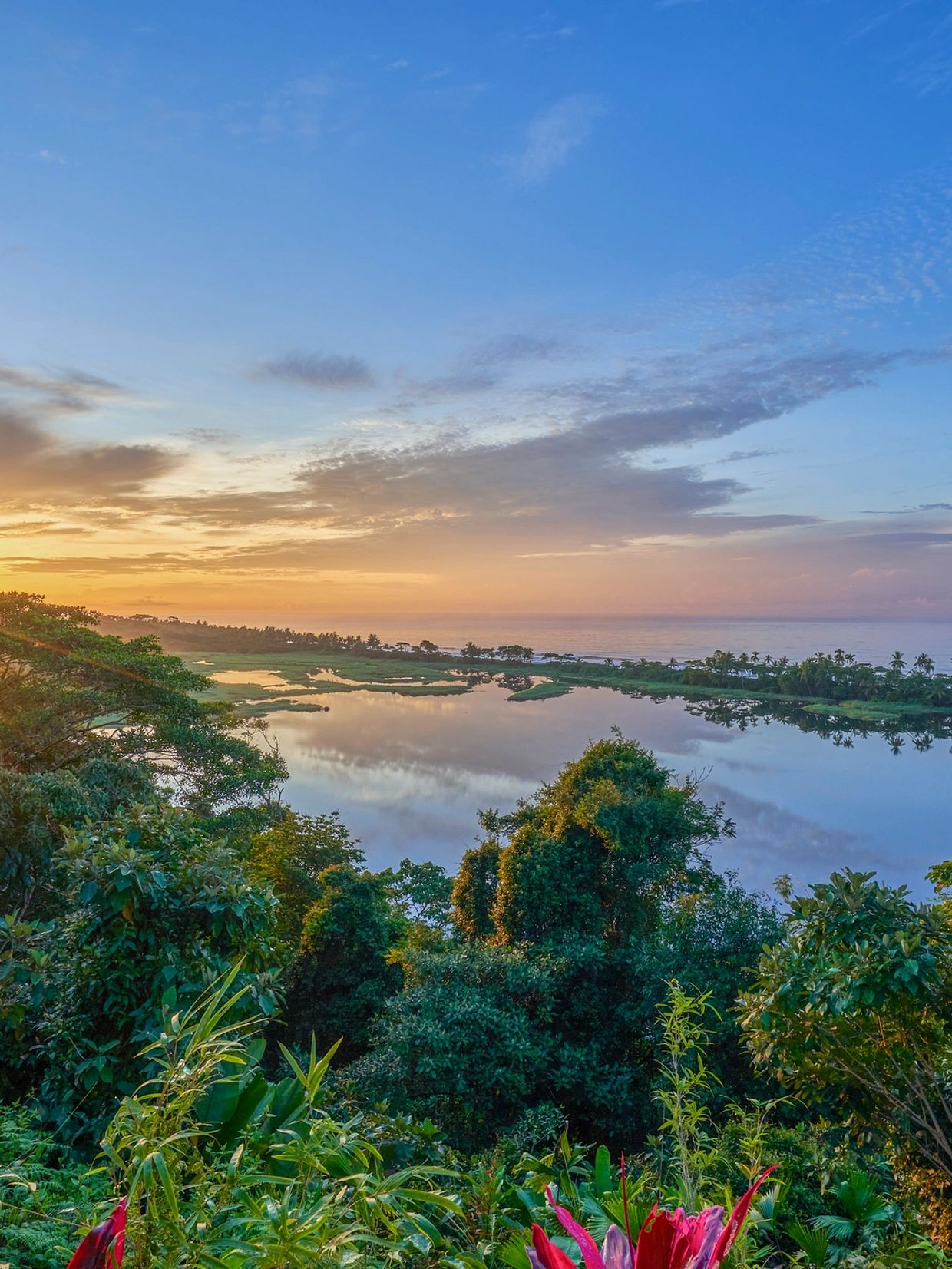 Sunset over a lush landscape with water reflecting the colorful sky.
