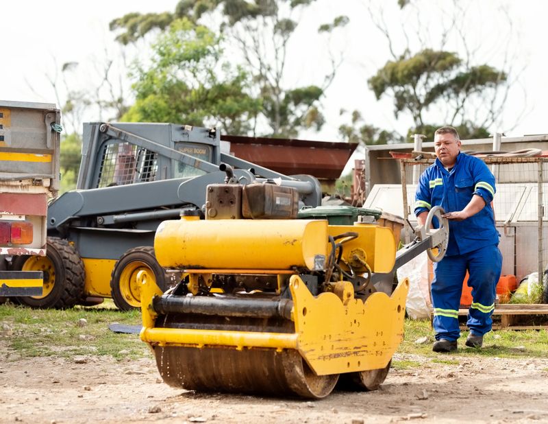 Male worker levelling the ground with heavy roller machine at construction site