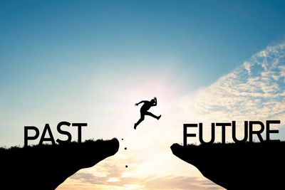 Silhouette of a person jumping from past to future over a gap.