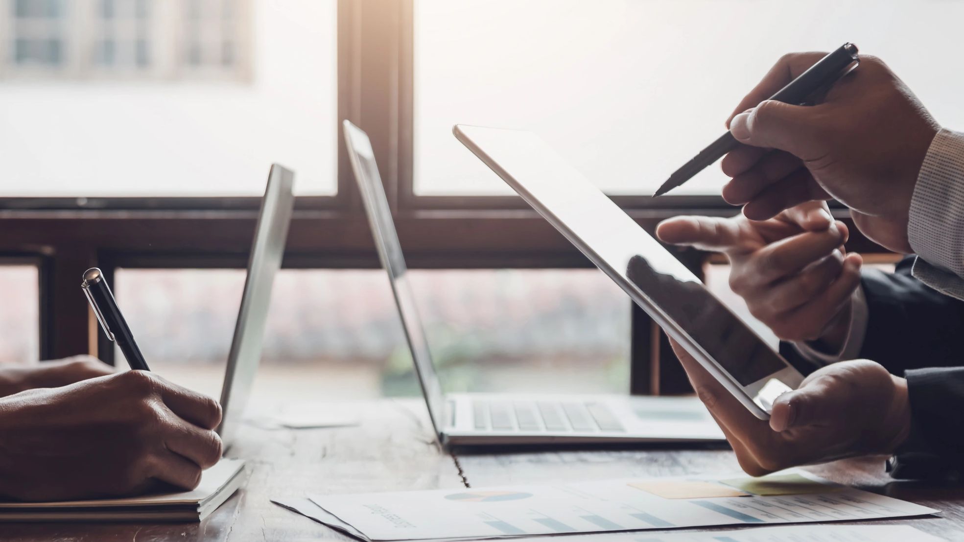 Business professionals collaborating using digital devices and paperwork at a meeting.