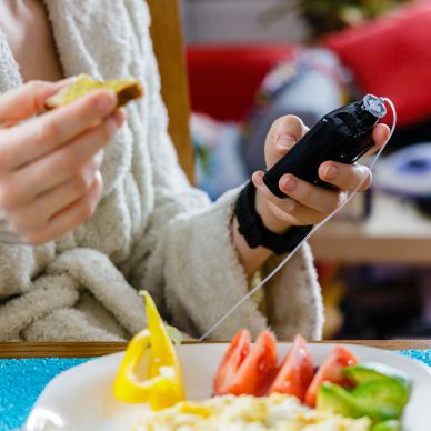 Person using a phone while eating a sandwich in a cozy setting.