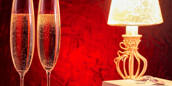 Two champagne flutes beside a lit decorative lamp and gift box on a table.