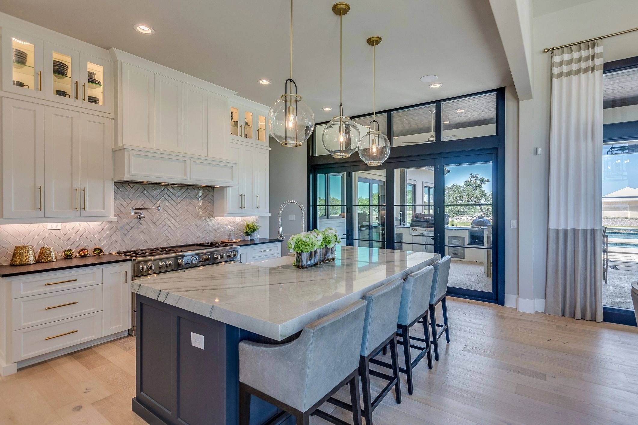 Modern kitchen with marble island and glass pendant lights.