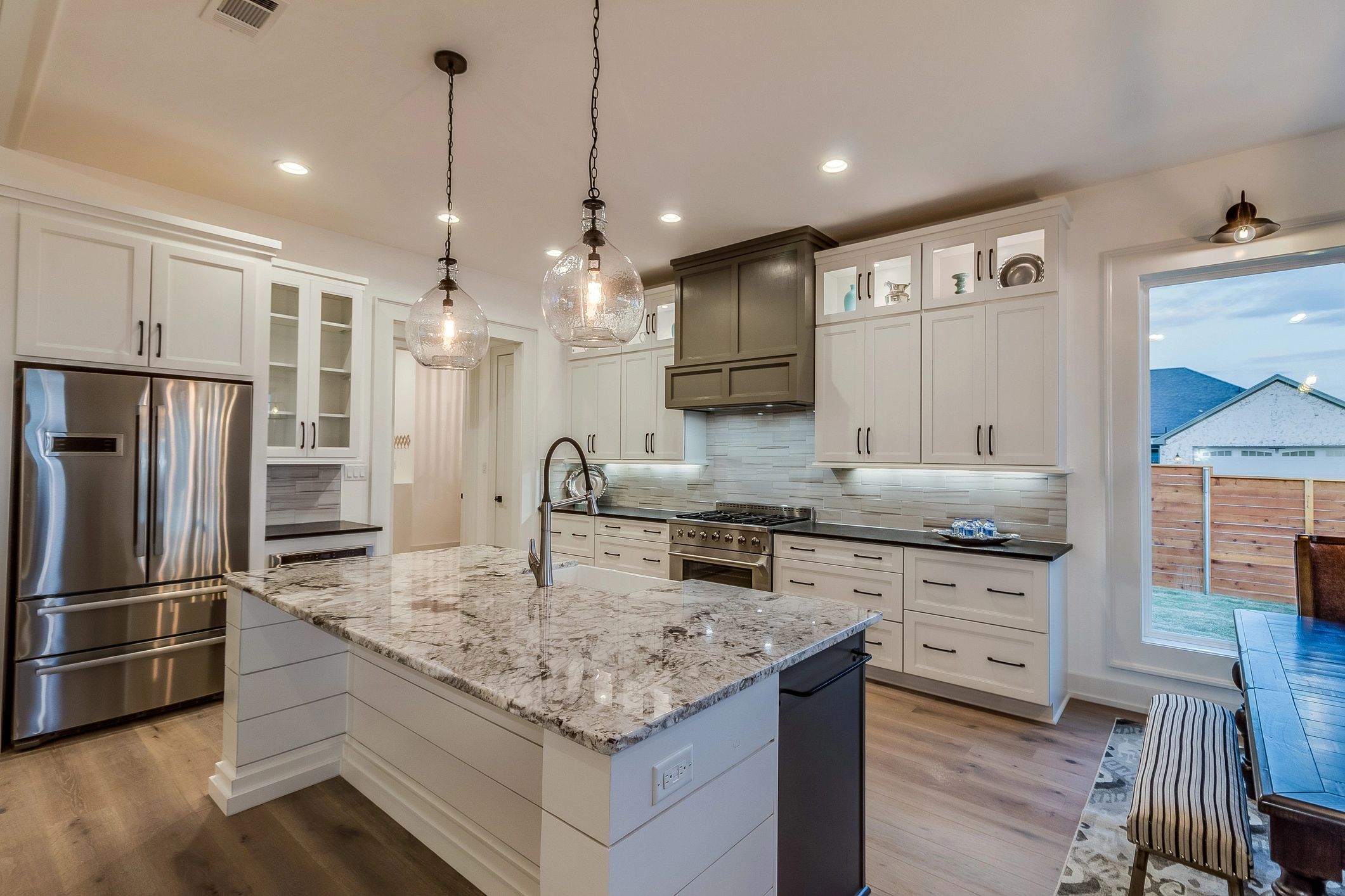 Modern kitchen with marble island, stainless steel appliances, and pendant lights.