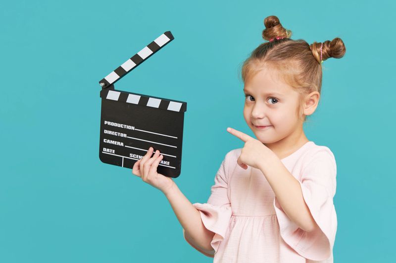 Funny smiling child girl hold film making clapperboard isolated on blue background. Little clipmaker, acting training. Funny face. Copy space for text."t