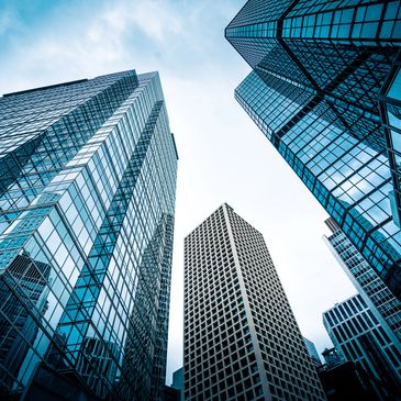 Looking up at tall modern skyscrapers with glass facades against a cloudy sky.