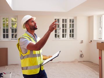 Construction worker inspecting a room interior with clipboard.