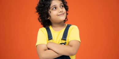 Young boy in yellow shirt and overalls smiling.