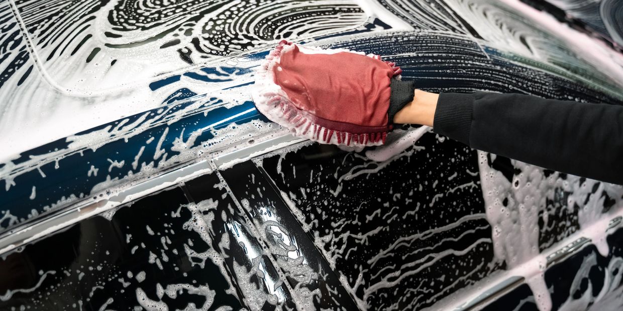 Person washing a car with a soapy mitt on a black vehicle.
