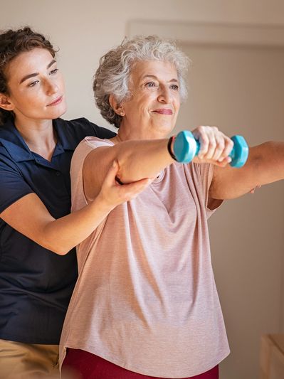 Elderly woman exercising with dumbbells guided by a fitness trainer.