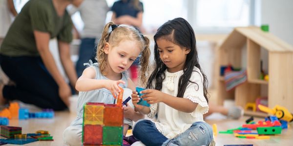 Two girls building with colorful magnetic tiles on the floor in a classroom.