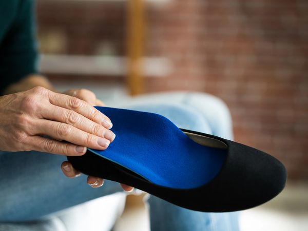 Person holding a black shoe with a blue orthotic insole inside.