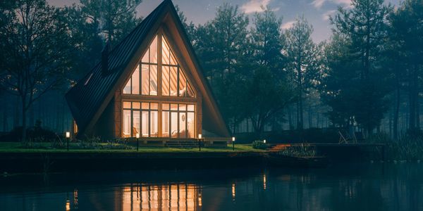 A glowing A-frame cabin by a calm lake under a starry night sky.