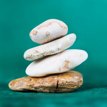 Stack of four smooth stones on a teal surface with a teal background.