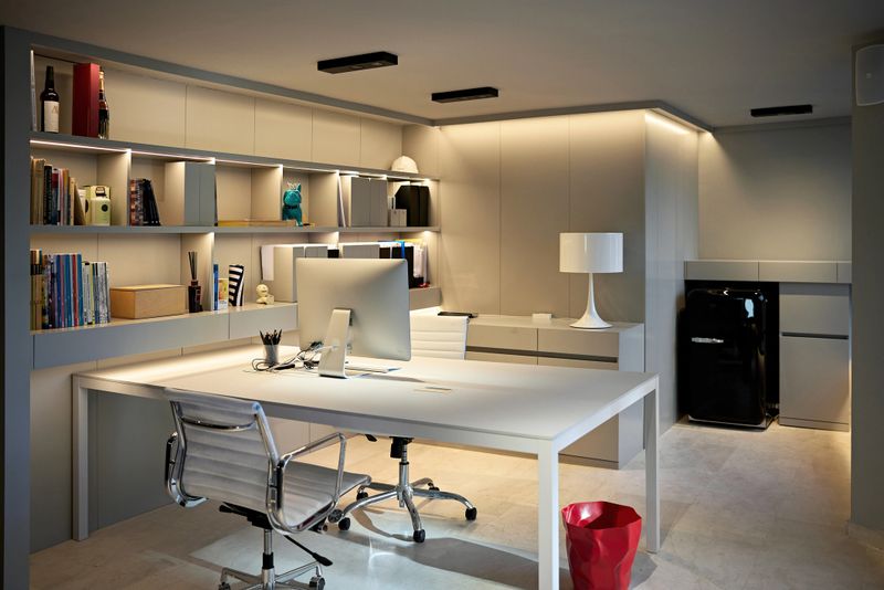 Unoccupied office area with desk, office chairs, desktop computer, bookshelves, recessed light, and stone flooring.